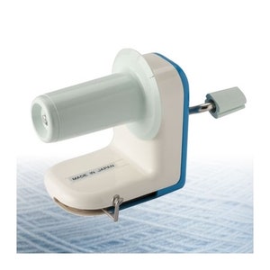 May include: White and blue yarn winder with a clear plastic bobbin. The winder has a handle and a metal hook. The label reads "Made in Japan".