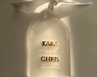 May include: White frosted glass ornament with gold lettering that reads "Our First Christmas Married" with the names "Kara and Chris" and the date "October 28, 2023" and location "Bonita Springs, FL".