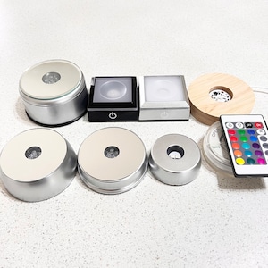 Puede incluir: Un conjunto de seis bases giratorias de exhibición plateadas con una parte superior de vidrio transparente. Las bases son de diferentes tamaños y vienen con un control remoto con múltiples opciones de color.