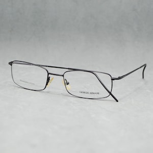 May include: Black rectangular eyeglasses with thin frames. The glasses have clear lenses and the brand name "GIORGIO ARMANI" is visible on the right lens. The frame material is stainless steel.