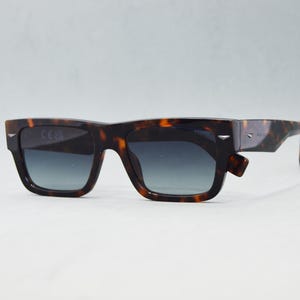 Puede incluir: Gafas de sol rectangulares con montura de patr&oacute;n de carey en marr&oacute;n y negro y lentes degradadas oscuras. La montura incluye detalles met&aacute;licos en tono plateado en las esquinas exteriores y a lo largo de las patillas.