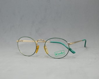 May include: Gold-rimmed round eyeglasses with green frames and clear lenses. The brand name "Benetton" is visible on the right lens.