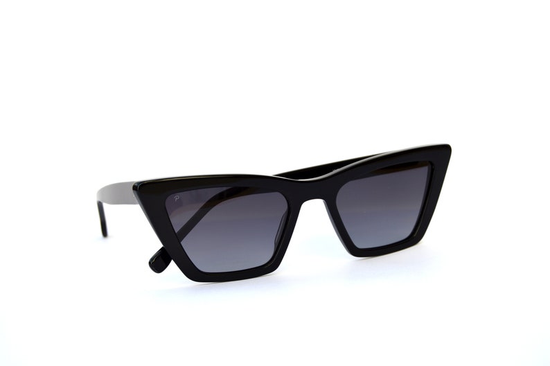 May include: Black cat-eye sunglasses with a sharp, angular frame and dark gray lenses.