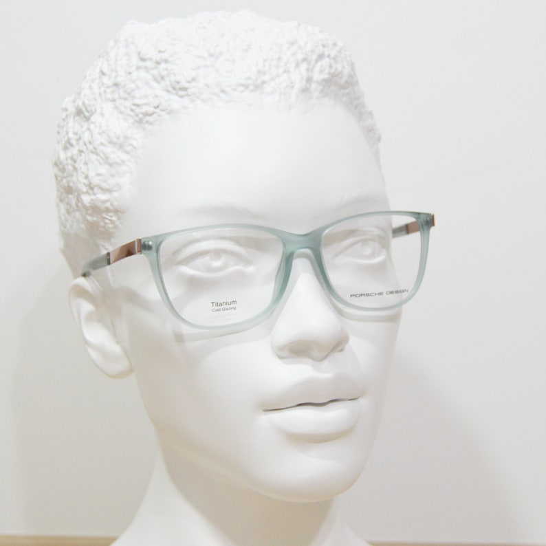 May include: A pair of light blue, semi-transparent eyeglasses with a silver frame. The frame is labelled "Titanium Cold Forming" on the left lens and "Porsche Design" on the right lens.