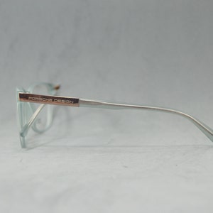 May include: A pair of light blue eyeglasses with a silver frame and rose gold accents. The frame has the text "PORSCHE DESIGN" on the side.