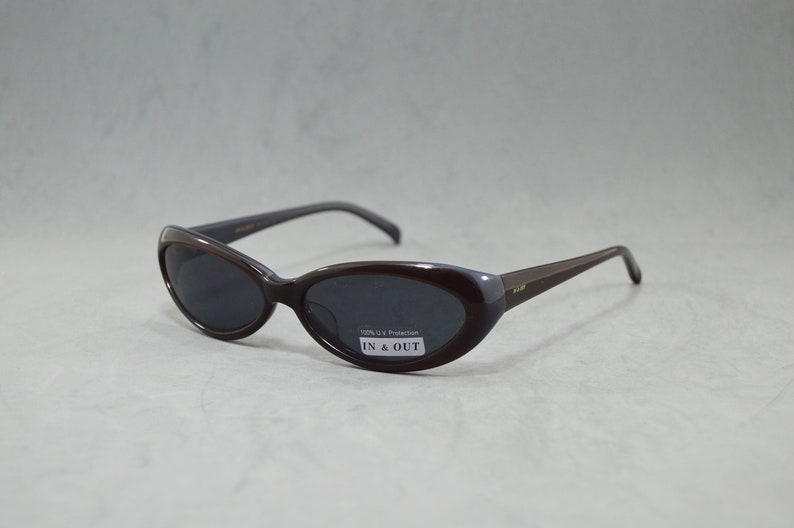 May include: Brown oval-shaped sunglasses with dark lenses. The sunglasses have a label that reads "100% UV Protection IN & OUT".