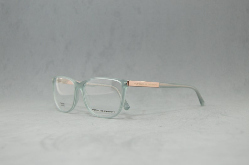 May include: A pair of light green eyeglasses with a rose gold frame and the text "PORSCHE DESIGN" on the side.