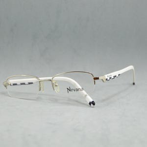 Könnte beinhalten: Weiße und silberne randlose Brille mit dem Wort "Nirvana" auf dem Rahmen.