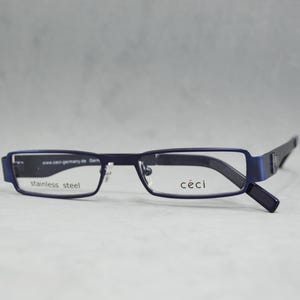 Puede incluir: Gafas rectangulares azules con montura de acero inoxidable y la palabra "ceci" impresa en la lente derecha.