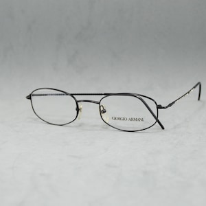 May include: Black metal frame eyeglasses with oval lenses. The brand name "Giorgio Armani" is printed on the right lens.