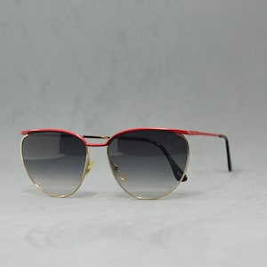 Könnte beinhalten: Rote und goldene Cat-Eye-Sonnenbrille mit dunkelgrauen Gläsern.