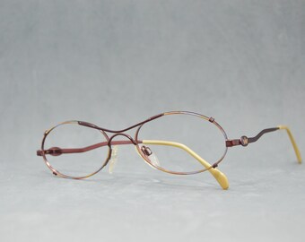 May include: A pair of brown oval-shaped eyeglasses with a thin metal frame. The arms of the glasses are a light brown color.