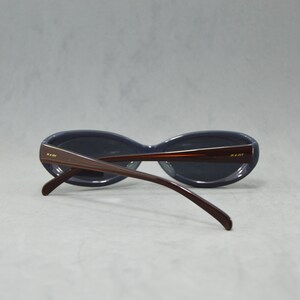 May include: A pair of dark blue oval-shaped sunglasses with brown plastic frames. The sunglasses have a gold logo on the side of the frames.