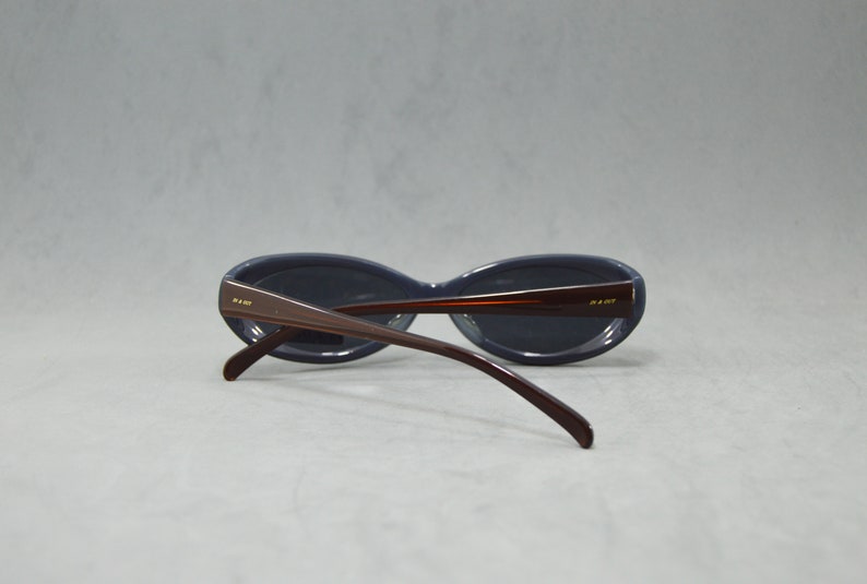 May include: A pair of dark blue oval-shaped sunglasses with brown plastic frames. The sunglasses have a gold logo on the side of the frames.