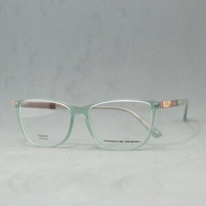 May include: A pair of light green spectacles with a gold accent on the arms. The frames are made of titanium and the lenses are clear. The text "Porsche Design" is printed on the right lens.