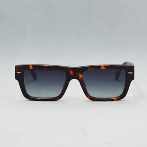 Puede incluir: Gafas de sol rectangulares con montura de patr&oacute;n de carey en marr&oacute;n y negro. Las lentes son oscuras y muestran un sutil tono degradado. Se aprecian peque&ntilde;os detalles met&aacute;licos en tono plateado en las esquinas exteriores de la montura.