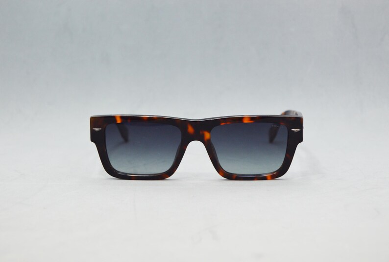 Puede incluir: Gafas de sol rectangulares con montura de patr&oacute;n de carey en marr&oacute;n y negro. Las lentes son oscuras y muestran un sutil tono degradado. Se aprecian peque&ntilde;os detalles met&aacute;licos en tono plateado en las esquinas exteriores de la montura.