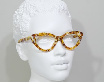 Könnte beinhalten: Eine Cat-Eye-Brille mit einem Schildpattmuster-Rahmen. Der Rahmen ist braun und gelb mit weißen Akzenten.