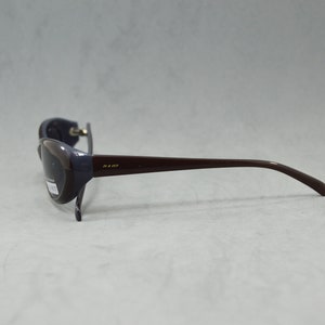 May include: A pair of dark brown sunglasses with a dark gray lens and a gold inscription on the side.