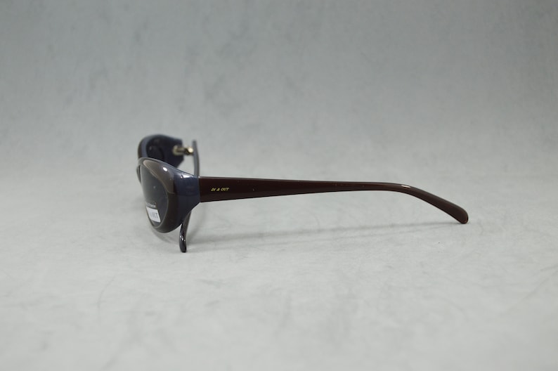 May include: A pair of dark brown sunglasses with a dark gray lens and a gold inscription on the side.