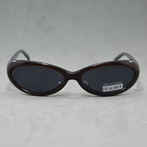 May include: Brown oval-shaped sunglasses with dark lenses. The sunglasses have a label that reads "100% UV Protection IN & OUT".