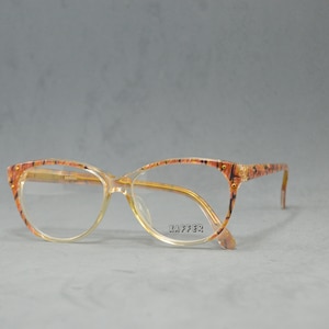 May include: A pair of brown and gold eyeglasses with a cat-eye frame. The brand name "Zaffer" is printed on the right lens.