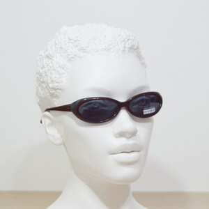 May include: A brown plastic oval-shaped sunglasses with dark lenses. The sunglasses have the text "IN & OUT" on the right lens.