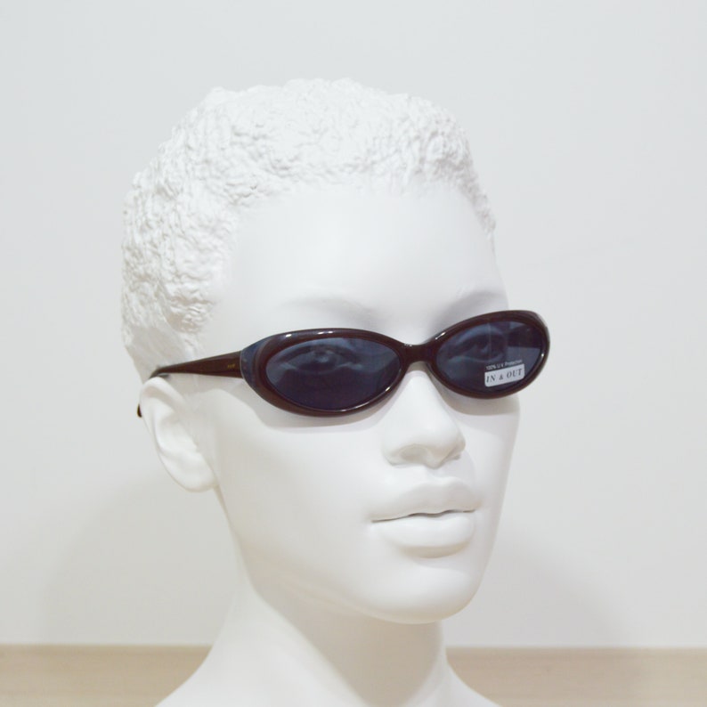 May include: A brown plastic oval-shaped sunglasses with dark lenses. The sunglasses have the text "IN & OUT" on the right lens.