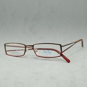 May include: Brown metal eyeglasses with red accents and clear lenses. The brand name "Blue Boy" is printed on the right lens.