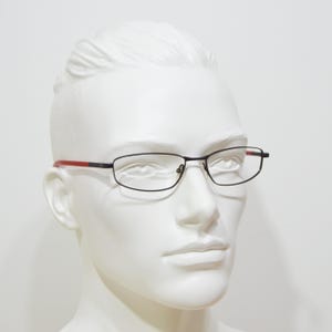May include: A black and red metal frame eyeglasses with clear lenses. The glasses are on a white mannequin head.