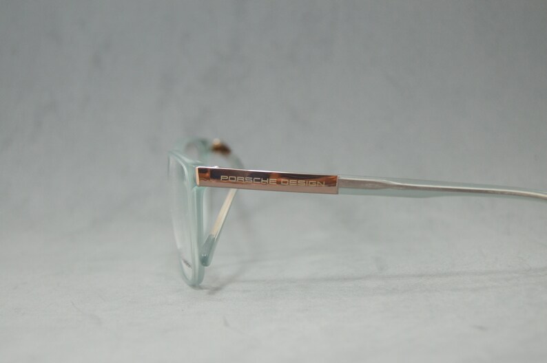 May include: A pair of light blue eyeglasses with a rose gold frame and the text "PORSCHE DESIGN" on the side.