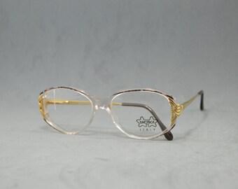 May include: Clear plastic oval-shaped eyeglasses with gold-tone accents and a black and gold "OPTICA ITALY" logo on the right lens.