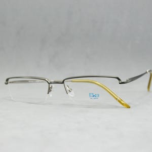 May include: Silver-toned metal eyeglasses with a gold-colored metal frame and clear lenses. The brand name "B.B. by Baby" is printed on the right lens.