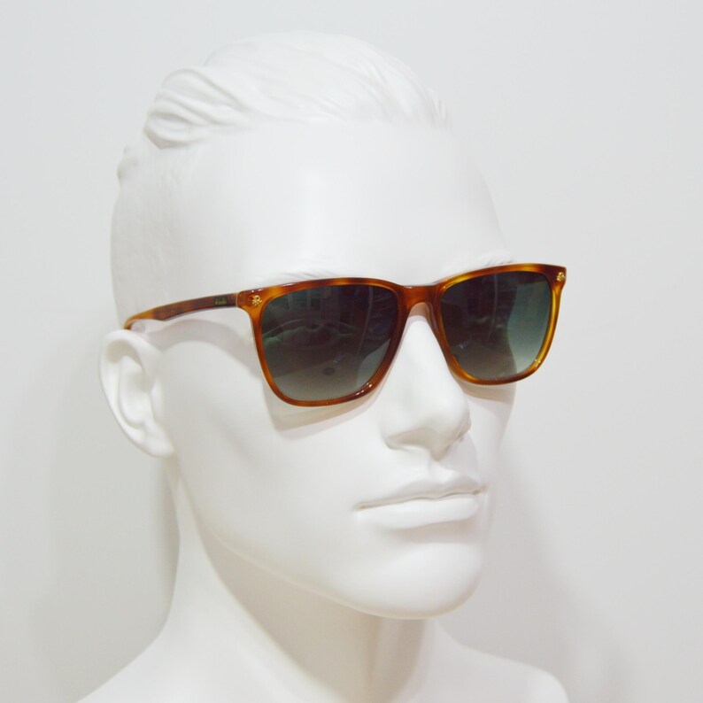 May include: Tortoise shell sunglasses with green tinted lenses. The sunglasses are on a white mannequin head.