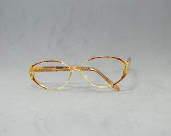 Könnte beinhalten: Eine ovale Brille mit einem braunen und goldenen Gestell. Das Gestell hat ein dezentes Muster und die Gläser sind klar.