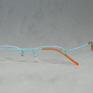 May include: A pair of rimless eyeglasses with a light blue metal frame and orange temple arms. The frame is labeled "Seventh Street".