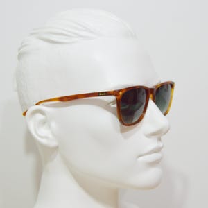 May include: Brown tortoise shell sunglasses with green lenses. The sunglasses are on a white mannequin head.