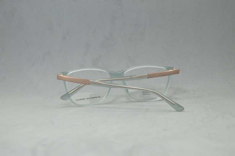 May include: Light blue eyeglasses with a rose gold frame. The frame has a silver metal bridge and arms.