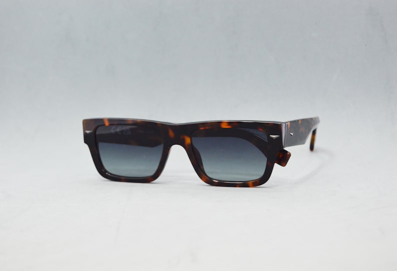 Puede incluir: Gafas de sol rectangulares con montura de patr&oacute;n de carey en marr&oacute;n y negro y lentes de color gris degradado. La montura gruesa de pl&aacute;stico incluye detalles met&aacute;licos en tono plateado en las esquinas exteriores y en las patillas.