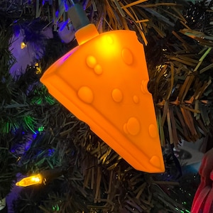 May include: A string of Christmas lights shaped like slices of cheese. The lights are lit and glowing yellow.