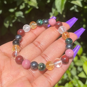 May include: A multi-coloured beaded bracelet with clear, red, pink, yellow, green, and black beads. The bracelet is worn on a person's wrist.