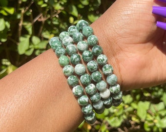 Puede incluir: Un conjunto de pulseras de cuentas de ágata verde y blanca. Las cuentas son redondas y tienen un patrón moteado.