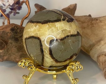May include: A polished, round, brown and yellow banded agate sphere on a gold metal stand. The sphere has a swirling pattern of brown and yellow bands.