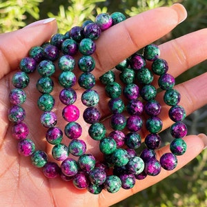 May include: A stack of green and pink gemstone bracelets. The bracelets are made of round beads with a speckled pattern.