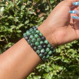May include: A stack of four green and black gemstone bracelets. The bracelets are made of round beads and are worn on a person's wrist.