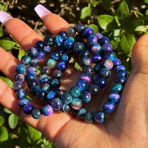 May include: Three stacked bracelets made of iridescent blue and green tiger's eye beads.