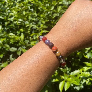 K&ouml;nnte beinhalten: Ein buntes Armband mit durchsichtigen, roten, violetten, braunen und gelben Perlen. Das Armband wird am Handgelenk getragen.
