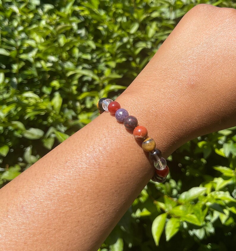 K&ouml;nnte beinhalten: Ein buntes Armband mit durchsichtigen, roten, violetten, braunen und gelben Perlen. Das Armband wird am Handgelenk getragen.