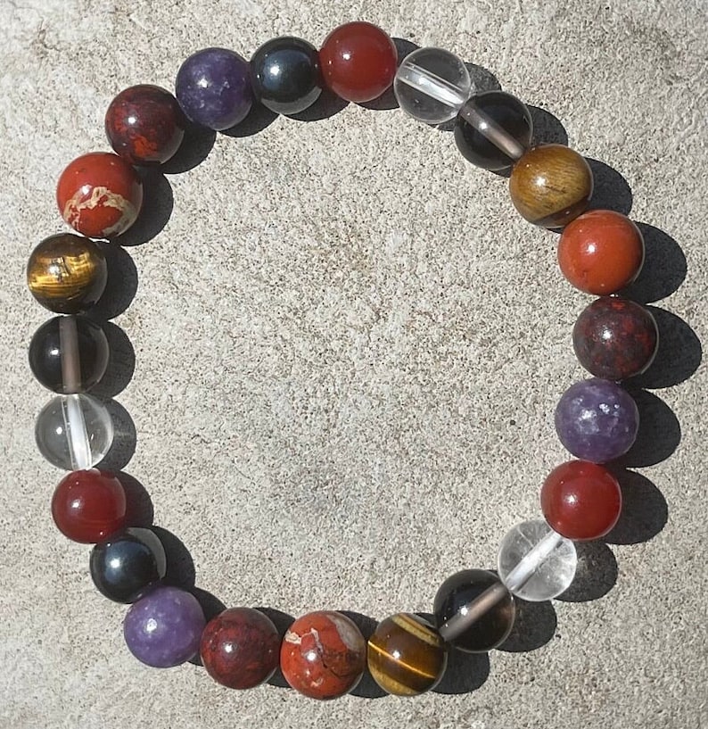 K&ouml;nnte beinhalten: Ein Armband aus verschiedenen Edelsteinen, darunter roter Jaspis, Tigerauge, H&auml;matit, Karneol, Amethyst und klarer Quarz.