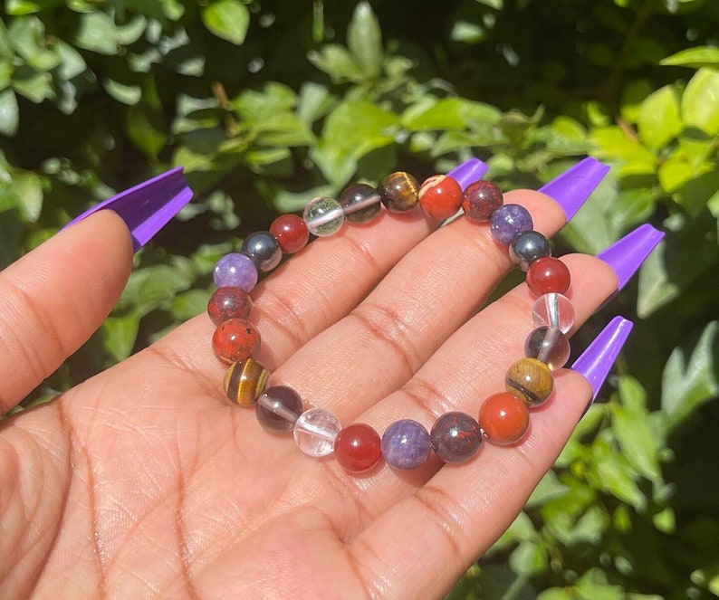 K&ouml;nnte beinhalten: Ein mehrfarbiges Armband mit roten, orangefarbenen, gelben, gr&uuml;nen, blauen und violetten Perlen. Das Armband besteht aus nat&uuml;rlichen Steinen und ist f&uuml;r das Tragen am Handgelenk gedacht.